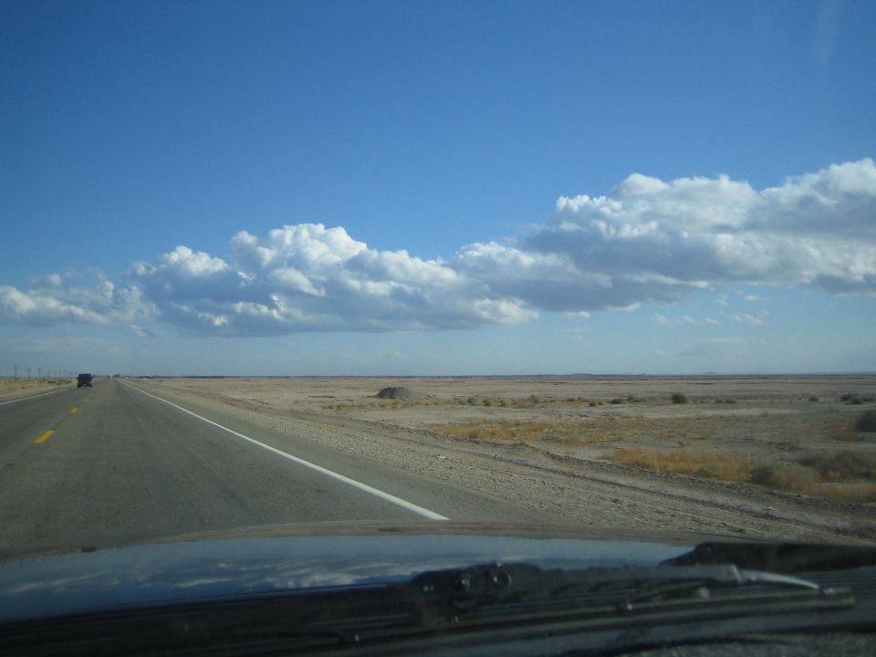 Straight desert highway under blue sky with scattered clouds and flat plains