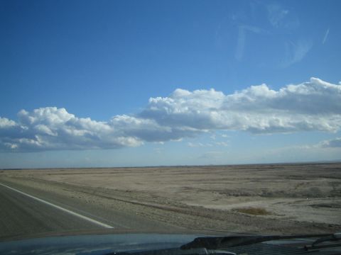 1990 Ford Bronco - wide flat desert plain stretches beside a highway under a broad blue sky banded with white clouds.
