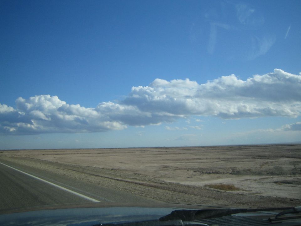Open desert plain beside a highway under a wide blue sky with white clouds