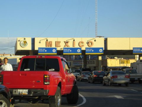 1990 Ford Bronco - red Ford Ranger pickup waits in line at a Mexican border crossing beneath large MEXICO declaration booths.