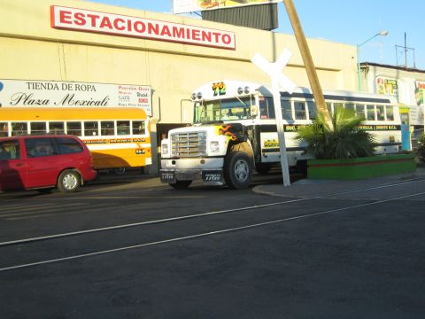 1990 Ford Bronco - white and yellow ex-school bus and a red minivan sit by a Plaza Mexicali storefront near railroad tracks.
