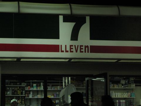 1990 Ford Bronco - illuminated 7-Eleven logo glows over a dim convenience store interior with stocked shelves and customers.