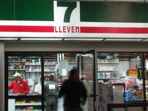 1990 Ford Bronco - Inside a 7-Eleven, staff in red shirts work behind the counter as a customer passes stocked shelves and coolers.