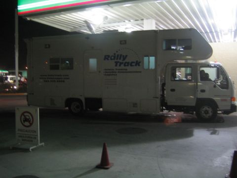 1990 Ford Bronco - white Rally Track motorhome built on a cab-over truck chassis sits under a gas station canopy at night.