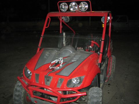 1990 Ford Bronco - red Yamaha side-by-side UTV with a roll cage, light bar, and graphic-decaled hood sits outdoors at night.