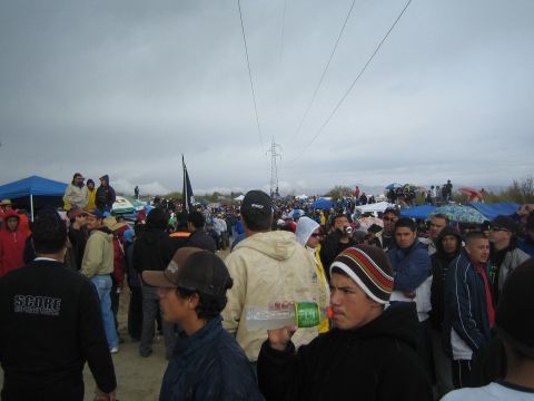 1990 Ford Bronco - dense crowd of spectators in jackets and caps fills the sandy ground beneath power lines and an overcast desert sky.