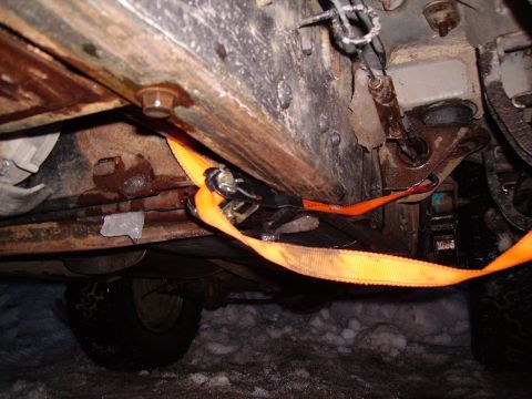 2000 Chevrolet Tahoe - An orange ratchet strap is secured to the rusty underside of a vehicle, with a tire visible in the snow.