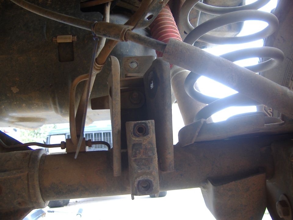 Close-up of a vehicle's rear axle, shock absorber, and coil spring assembly. Some brake lines are visible