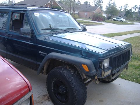 2004 Jeep Wrangler - A dark green Jeep Cherokee Sport shows damage to its front bumper and is parked next to a red vehicle.