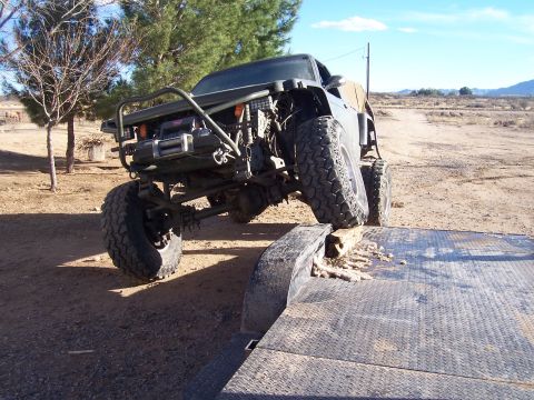 1981 Ford F-150 - This heavily modified truck is being loaded onto a trailer, showing its lifted suspension and off-road tires.