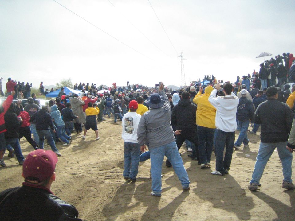 Crowd of spectators spread across sandy hillside watching a desert race