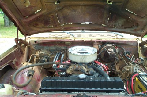 1978 Dodge Power Ram - The engine bay of a weathered truck reveals a V8 engine beneath the open hood, with visible hoses and wiring.