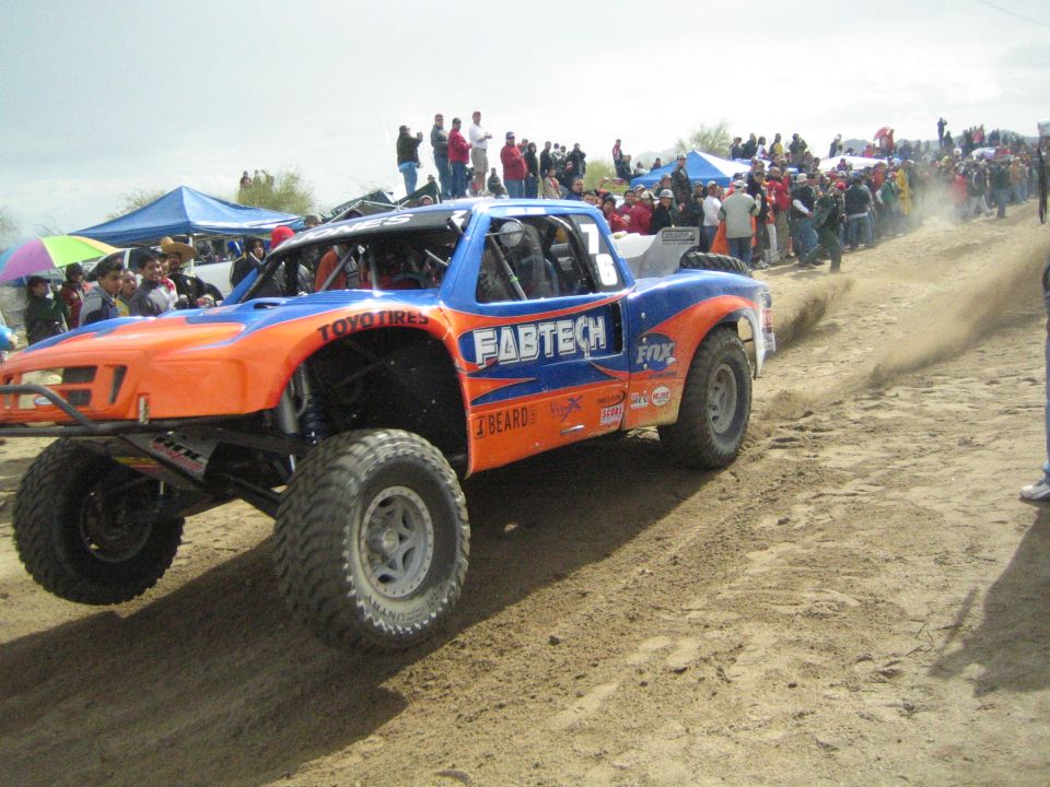Orange and blue Fabtech off-road trophy truck on a sandy course