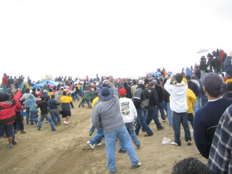 1990 Ford Bronco - dense crowd of jacketed spectators spreads across a sandy desert clearing dotted with pop-up tents.