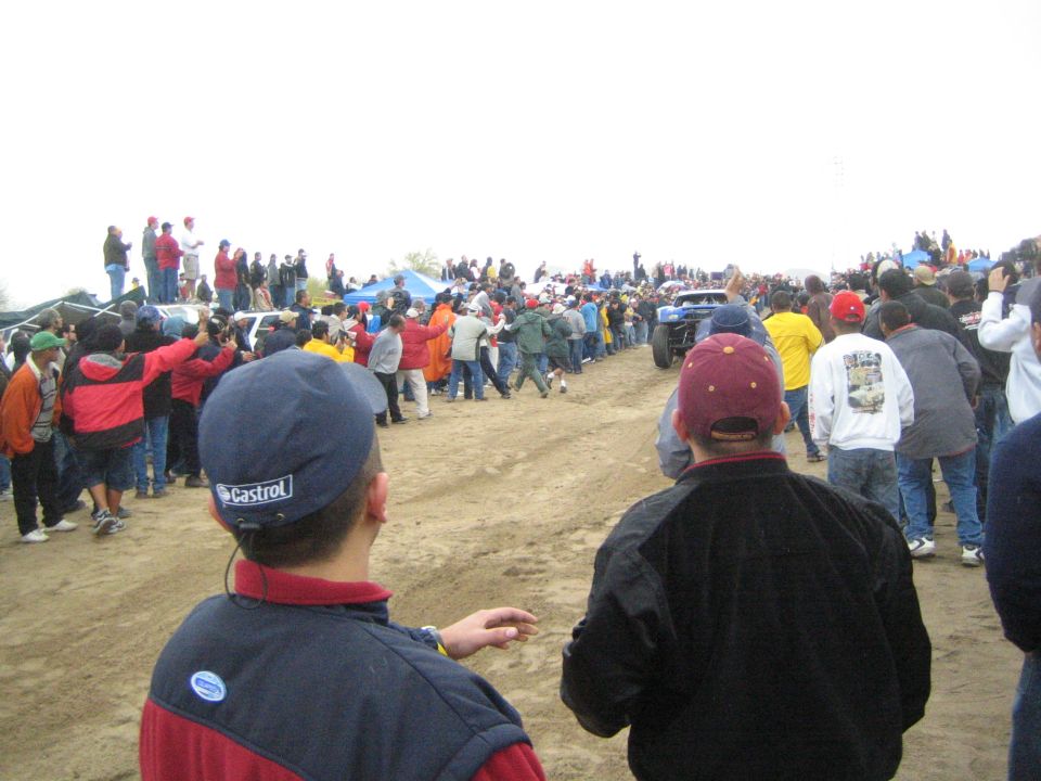 Spectators in caps watching a distant truck on a sandy course