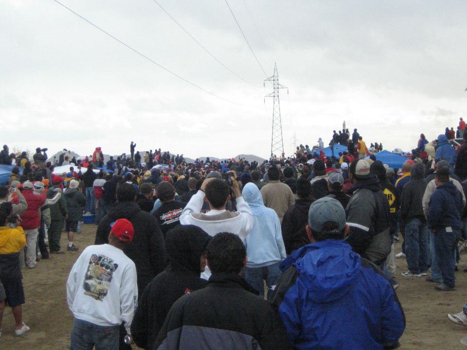Dense crowd of spectators facing a distant power-line tower