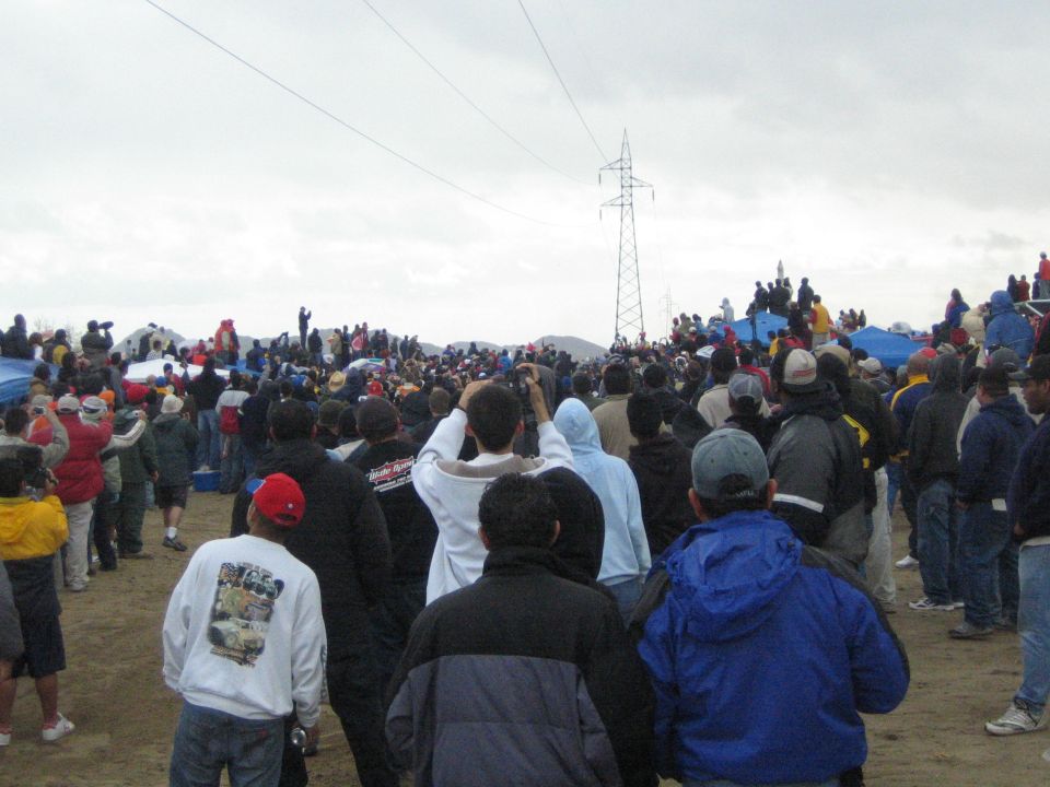 Spectators in winter clothing watching across a sandy desert field