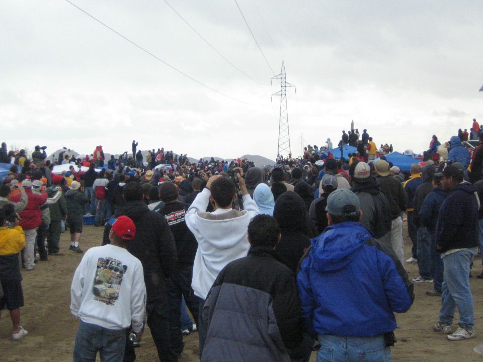 Crowd of spectators gathered on sandy ground under a cloudy sky