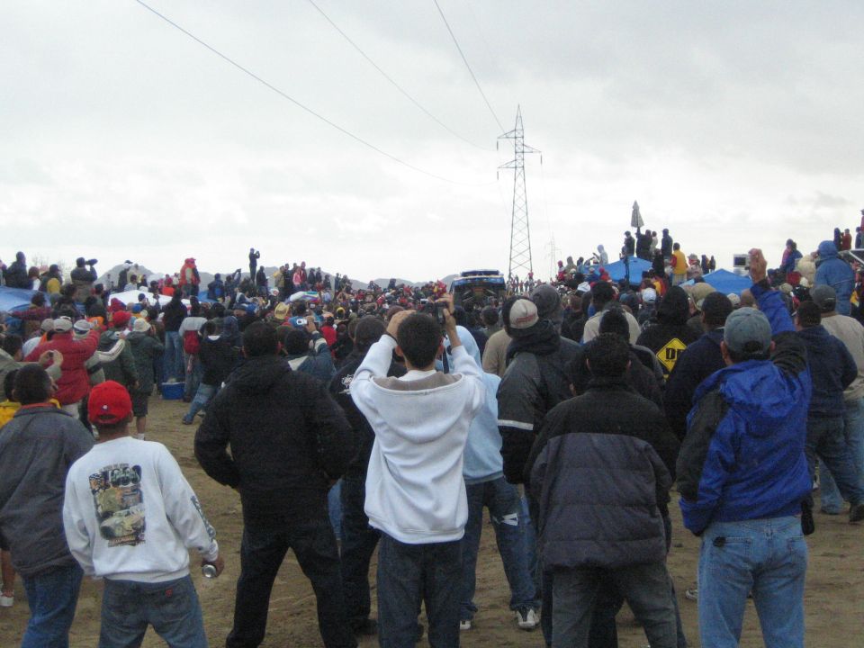 Crowd of spectators with a white truck visible across the sand