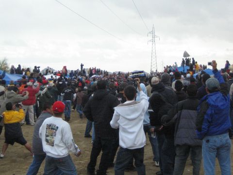 1990 Ford Bronco - Spectators in winter jackets gather on sandy ground near a white vehicle and pop-up tents under a cloudy sky.