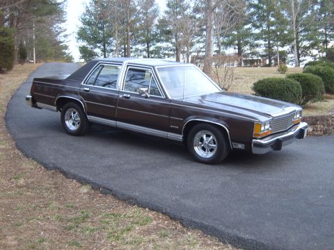 1982 Ford Crown Victoria LTD - A dark brown sedan with chrome accents and aftermarket wheels sits on a paved driveway surrounded by trees.