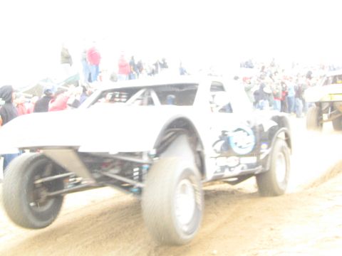 1990 Ford Bronco - blurry, overexposed action shot captures a white tube-frame off-road race buggy throwing dust before a crowd of spectators.