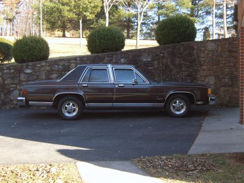 1982 Ford Crown Victoria LTD - A side view of a brown sedan with chrome trim and aftermarket wheels is parked on asphalt.