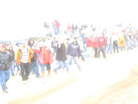 1990 Ford Bronco - bright, washed-out photo shows a crowd of jacketed spectators walking and gathering along a sandy desert course.