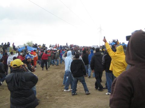 1990 Ford Bronco - large crowd of spectators in cold-weather jackets gathers on a sandy desert course beneath power lines on an overcast day.