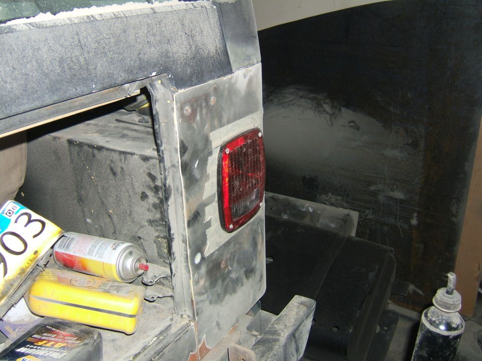 Bare metal Jeep rear corner with red tail light during fabrication work