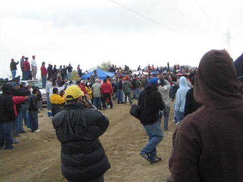 1990 Ford Bronco - crowd of spectators mingles near parked cars and a blue canopy along a sandy desert course on an overcast day.