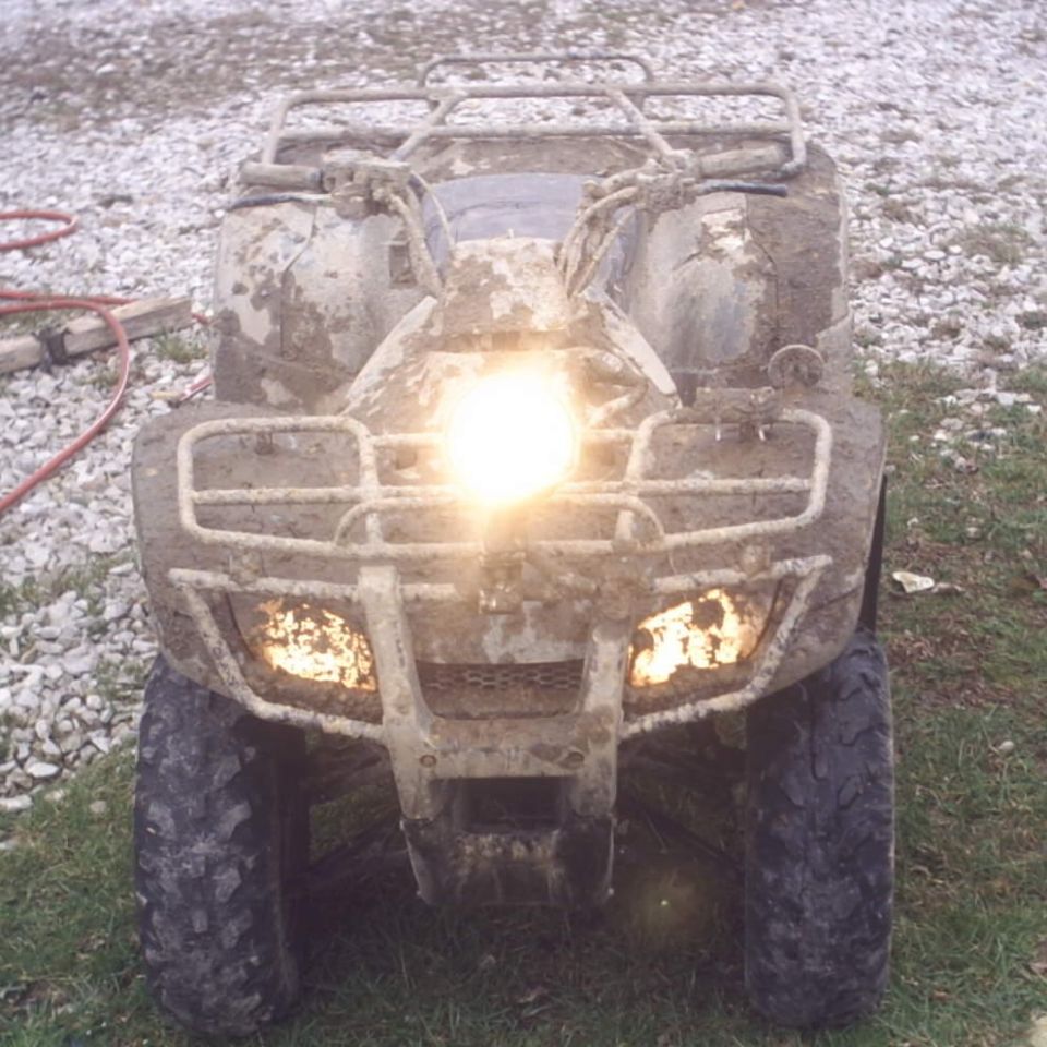Muddy ATV front view with headlights on