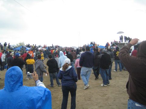 1990 Ford Bronco - large crowd of spectators walks and gathers across a sandy desert course beneath power lines on an overcast day.