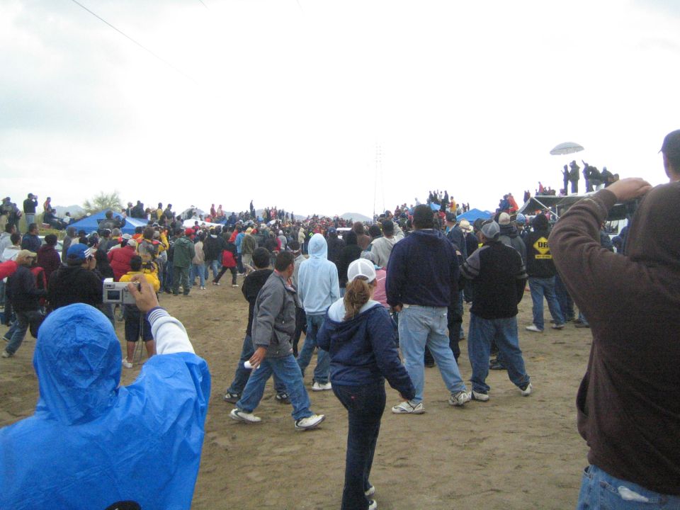 Crowd walking across a sandy course toward distant gathered spectators