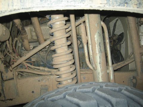 1990 Ford Bronco - Close-up of a dust-covered coil spring, suspension links and mud tire beneath an off-road vehicle.