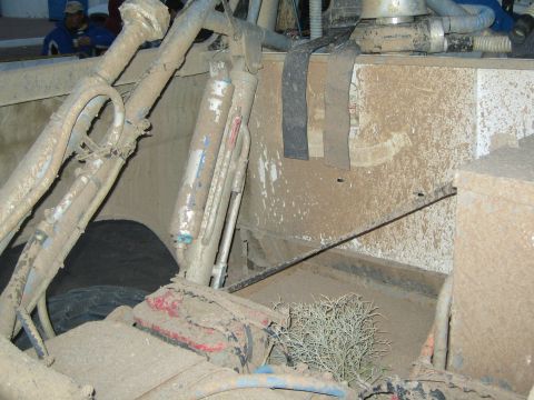 1990 Ford Bronco - Heavily mud-caked interior tubing and bed area of an off-road race vehicle, with dried brush stuck on.