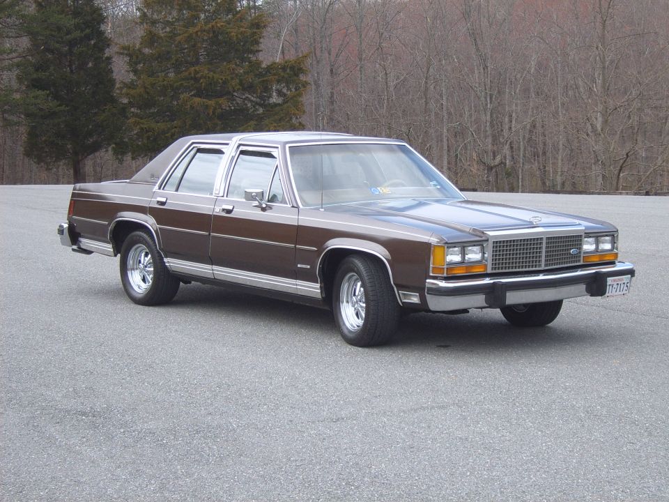 Brown Ford LTD Crown Victoria four-door sedan on empty asphalt lot, front three-quarter view