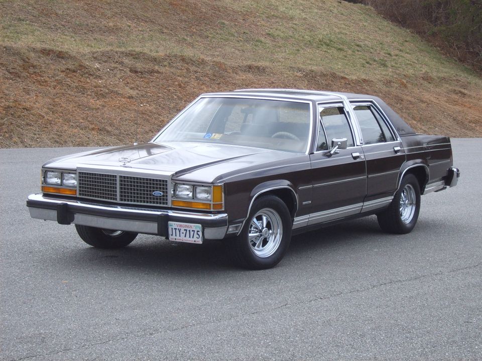 Brown Ford full-size sedan, 3/4 front view on pavement, chrome grille and polished five-slot wheels