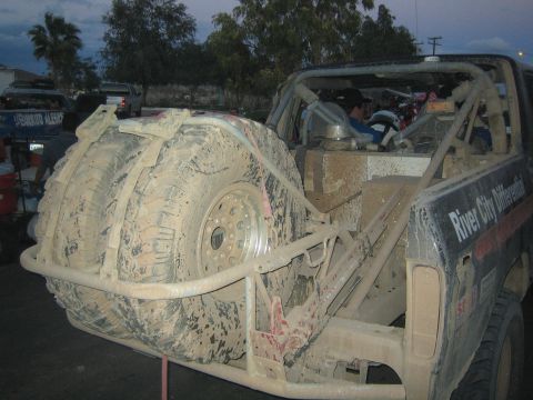 1990 Ford Bronco - Rear of a mud-caked off-road race truck carrying two spare tires on a tube bumper, marked River City Differential.