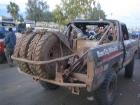 1990 Ford Bronco - Rear three-quarter view of a mud-covered off-road race truck with dual spare tires and River City Differential decal.