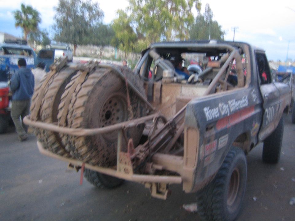 Rear three-quarter view of a muddy off-road truck with dual spare tires at dusk