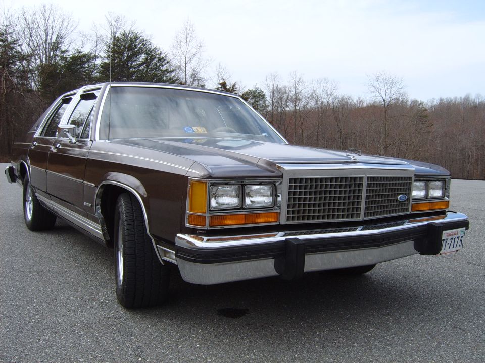 Brown Ford LTD Crown Victoria sedan, low front three-quarter view, bare trees behind