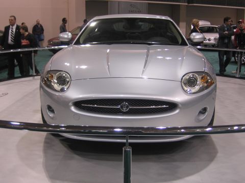 1999 Ford Crown Victoria - A silver Jaguar XK is displayed at an auto show, its distinctive front grille and headlight design.