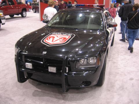 1999 Ford Crown Victoria - Black police car with push bumper and ram logo on hood, seen at an auto show.