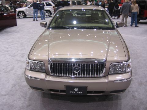 1999 Ford Crown Victoria - A tan Mercury Grand Marquis is displayed at an auto show, its distinctive grille and headlights.