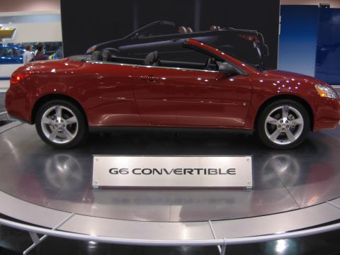 1999 Ford Crown Victoria - Red convertible displayed on a turntable with a sign identifying it as a G6 Convertible.