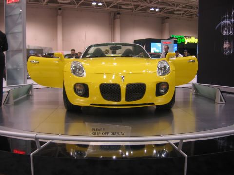 1999 Ford Crown Victoria - A bright yellow convertible is displayed with its doors open at an auto show.
