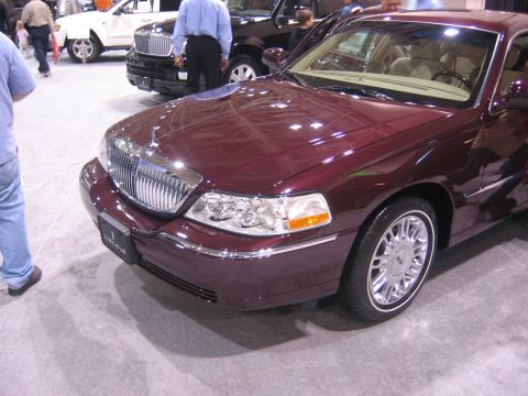 1999 Ford Crown Victoria - A maroon Lincoln Town Car is displayed at an auto show with other vehicles in the background.