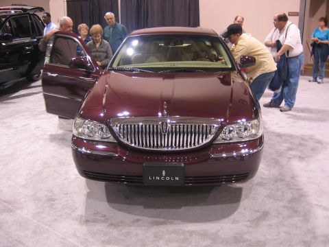 1999 Ford Crown Victoria - A maroon Lincoln Town Car is displayed at an auto show with people looking at it.