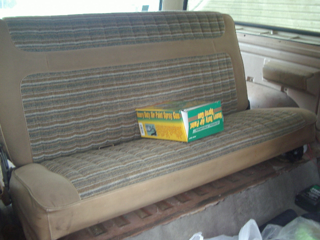 Rear bench seat with striped fabric and a box of spray paint on it